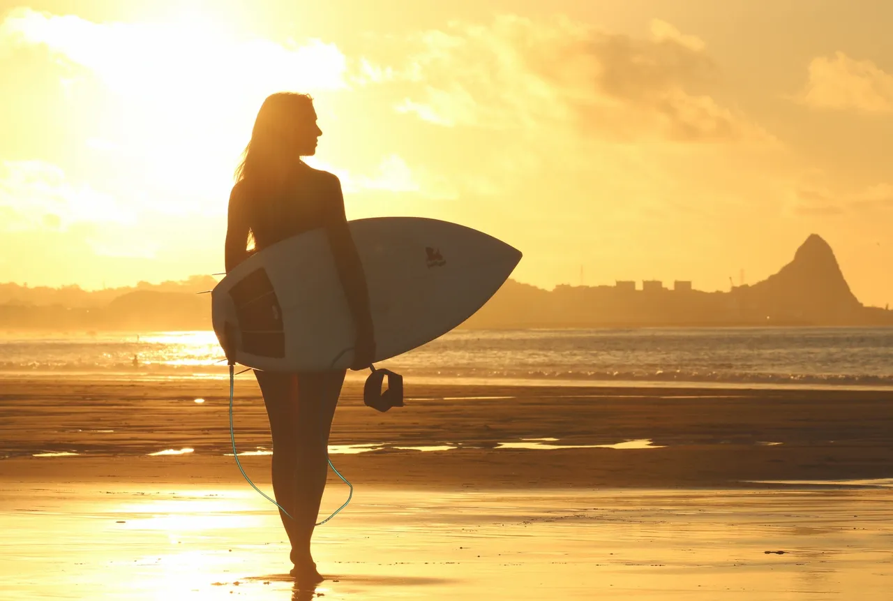 A woman holding a surfboard while standing on the beach.
