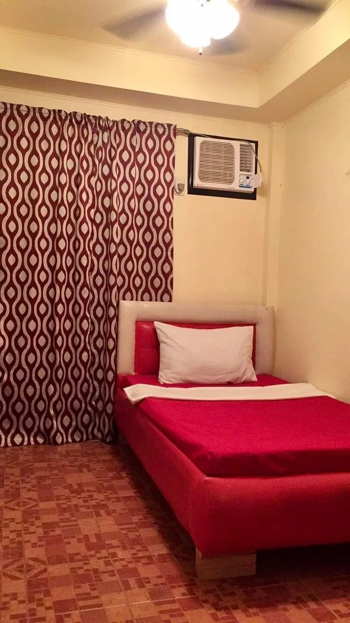 A red bed in a room with curtains and a window.
