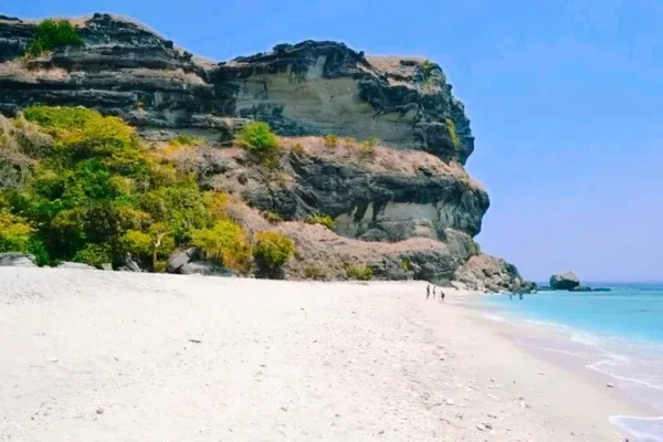 A beach with people walking on it and some rocks