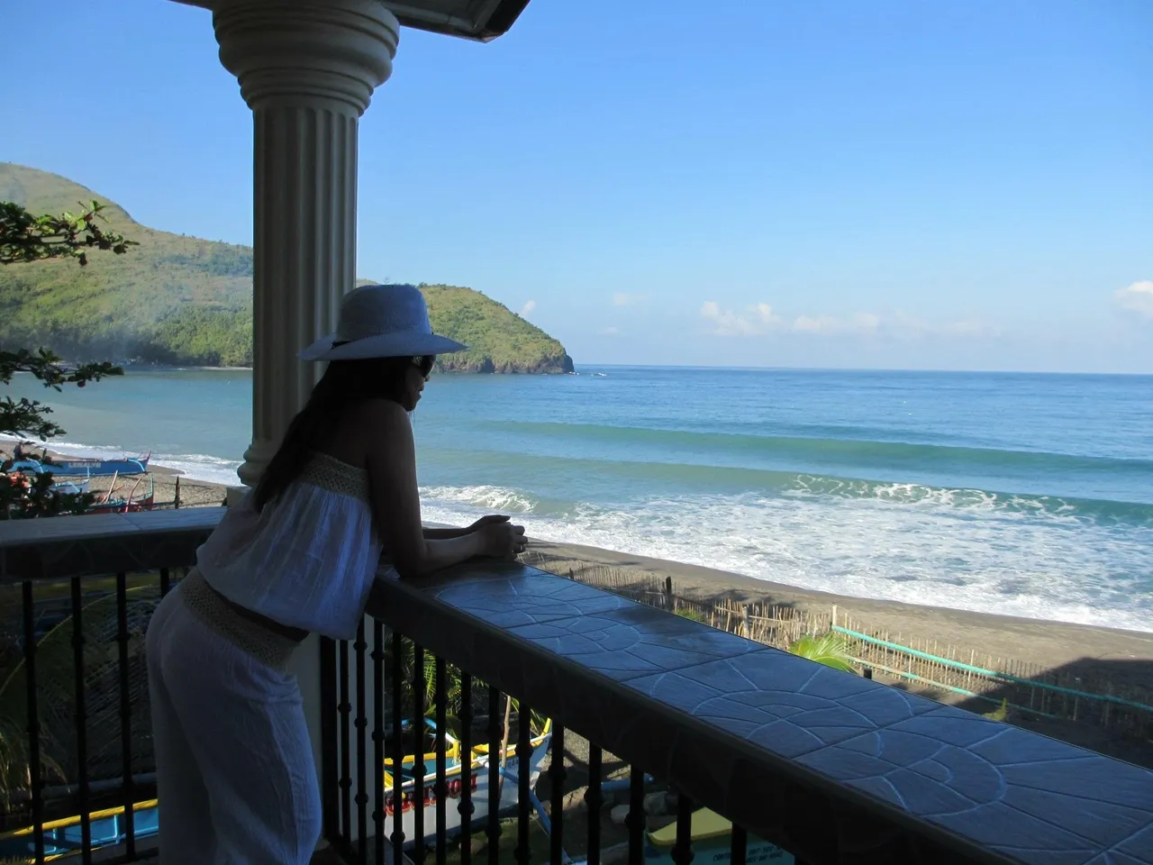 A woman standing on the balcony of her hotel room looking out at the ocean.